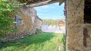 A stone building with a wooden structure on the right, a grassy area, and a clear sky.