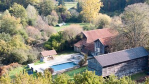 A rustic barn with a swimming pool and outdoor seating area surrounded by trees.