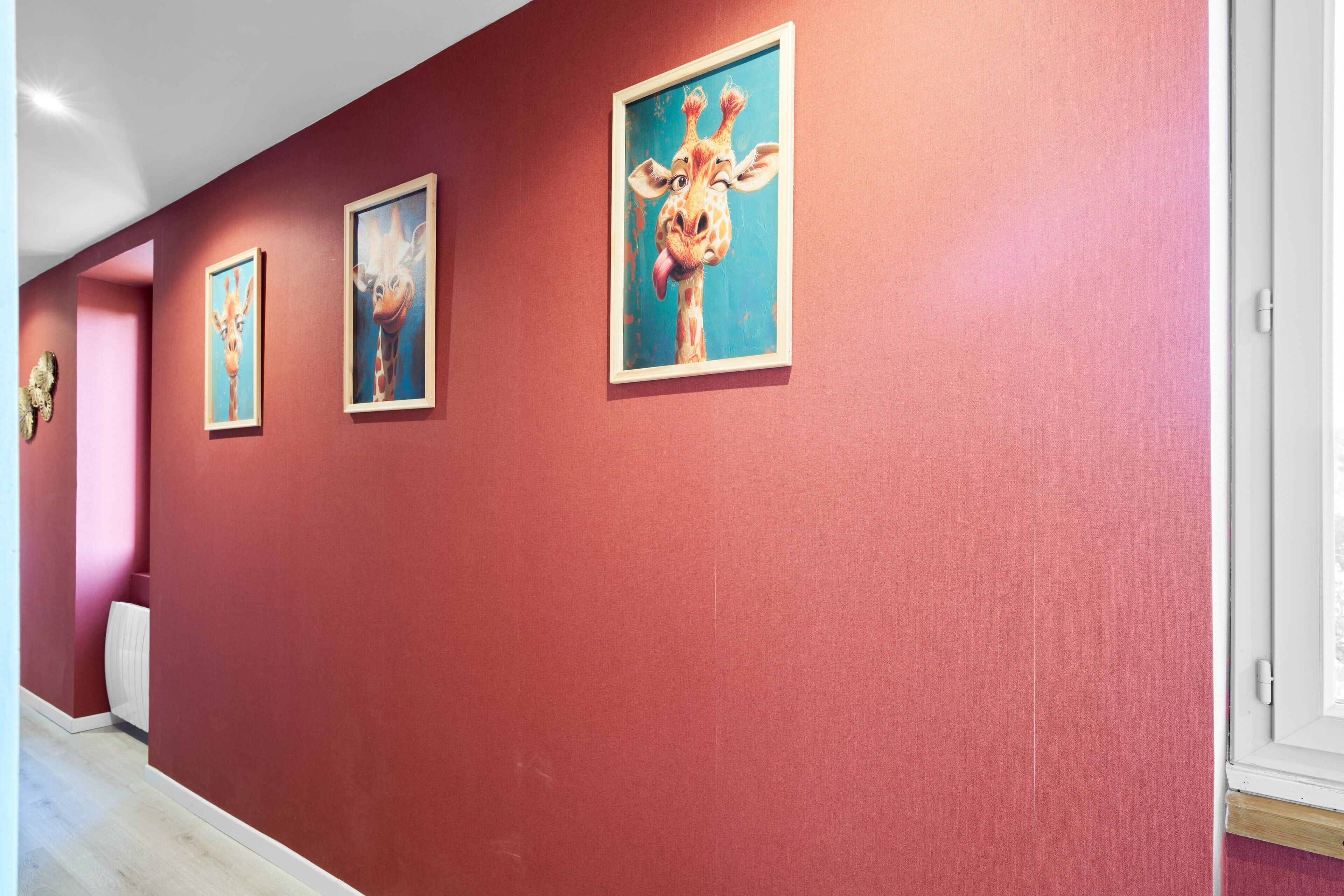 A hallway with red walls and framed artwork, including a giraffe painting.