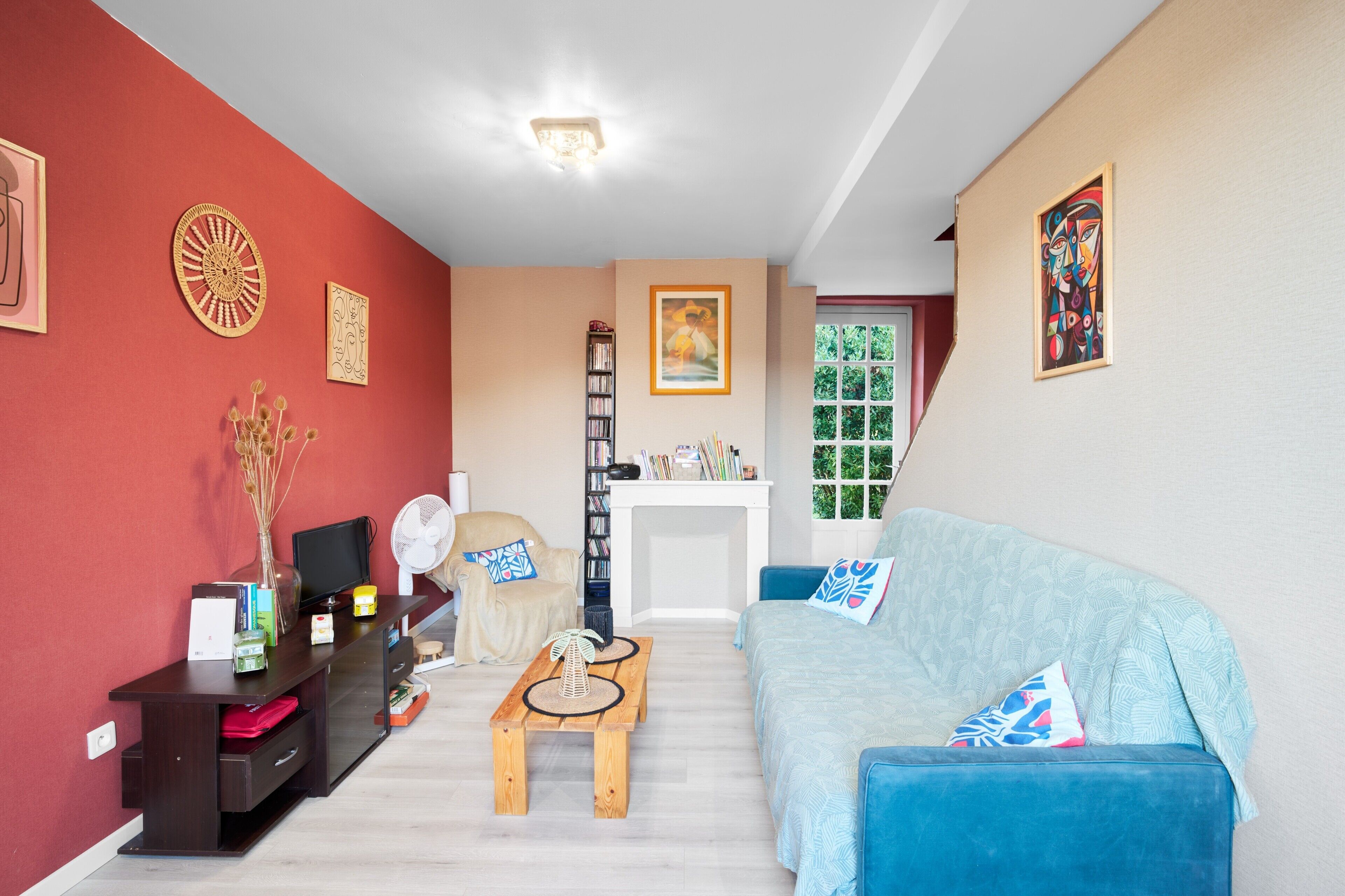 A living room with a red wall, a blue sofa, a wooden coffee table, a bookshelf, and a fireplace.