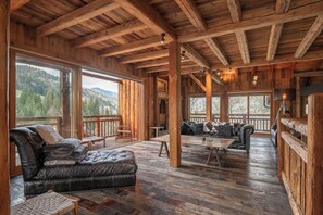 Une cabane en bois spacieuse, dotée d’un grand salon, d’un canapé, d’une table et d’un balcon offrant une vue sur les montagnes.