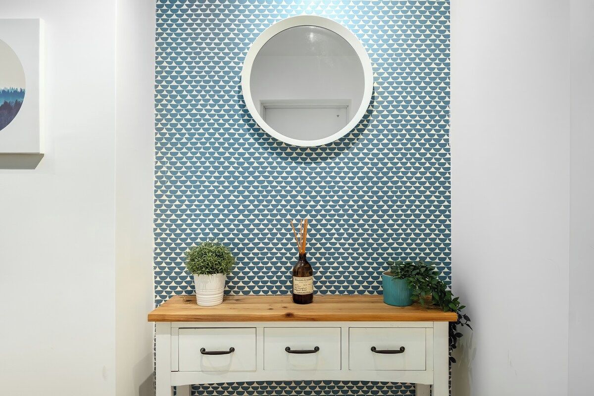 A bathroom with a white vanity, a round mirror, and a patterned wall.