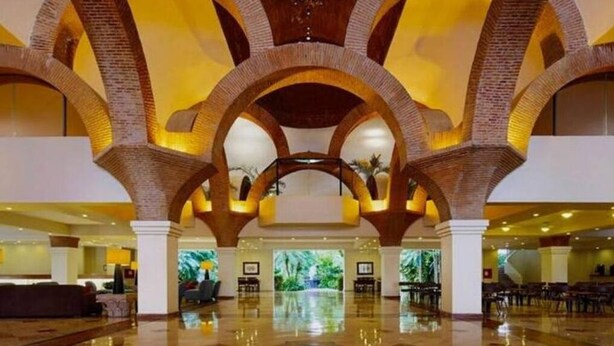 A spacious lobby with high ceilings and arched brick columns, featuring a polished floor and a large digital screen displaying a tropical scene.