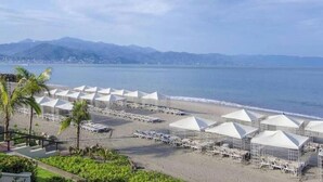 A beach with rows of white tents and lounge chairs, a clear view of the sea, and distant mountains.