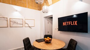 A modern conference room with a round wooden table, black chairs, a black TV screen displaying "NETFLIX", and framed abstract art on the wall.