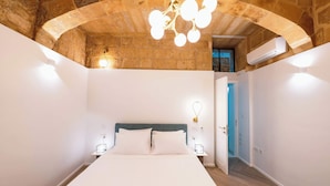 Un dormitorio con techo abovedado de piedra, una cama con ropa blanca y una lámpara de araña moderna.