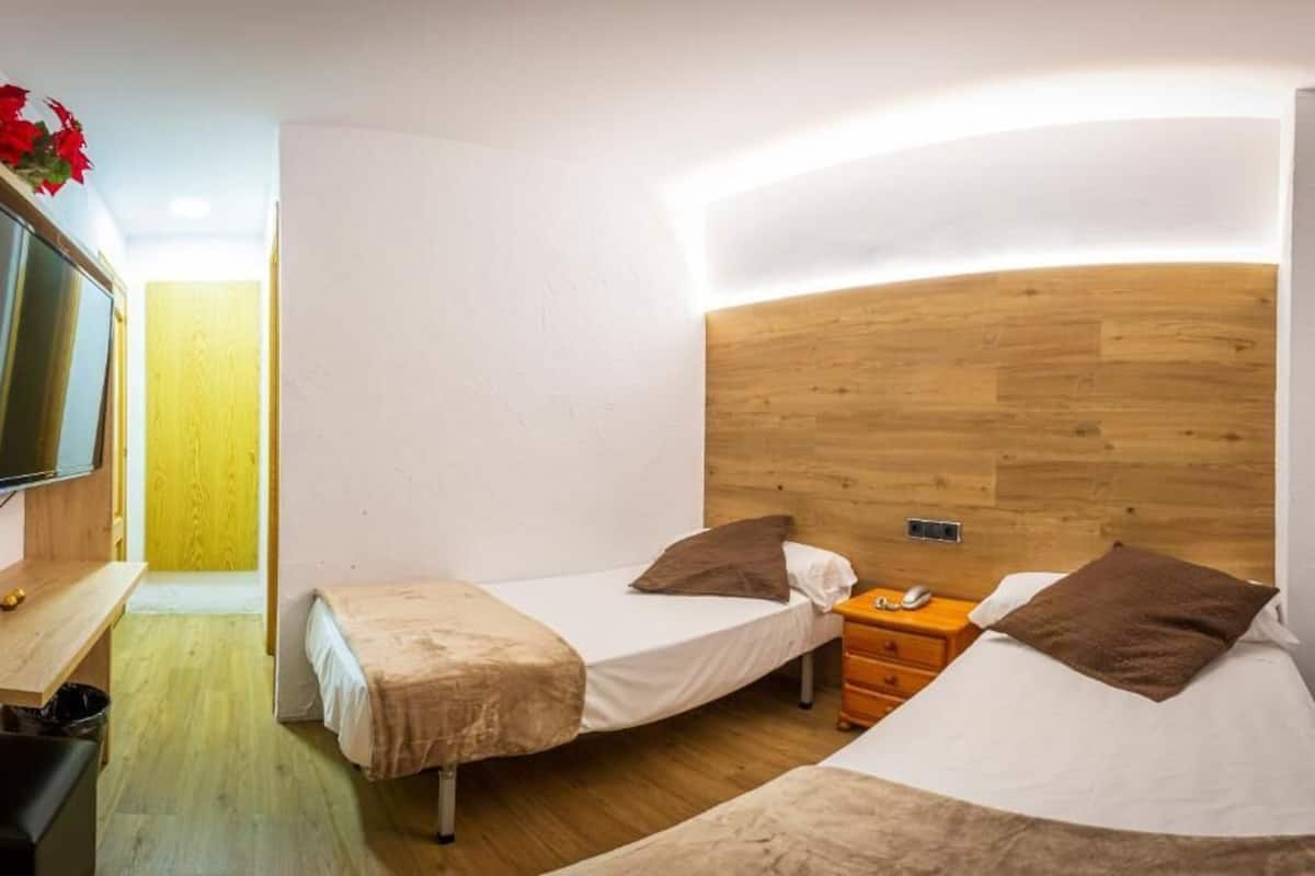 Ein kompaktes Hotelzimmer mit zwei Einzelbetten, einem Holzkopfstück, einem kleinen Schreibtisch und einem Fernseher.