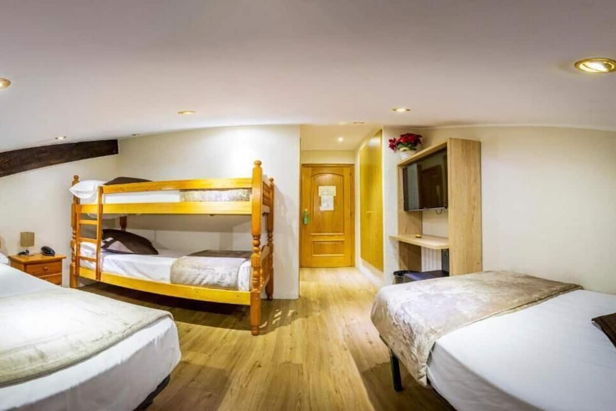 Ein Zimmer mit zwei Einzelbetten, einem Etagenbett, einem Holzschrank, einem Fernseher und einer Tür zu einem weiteren Raum.