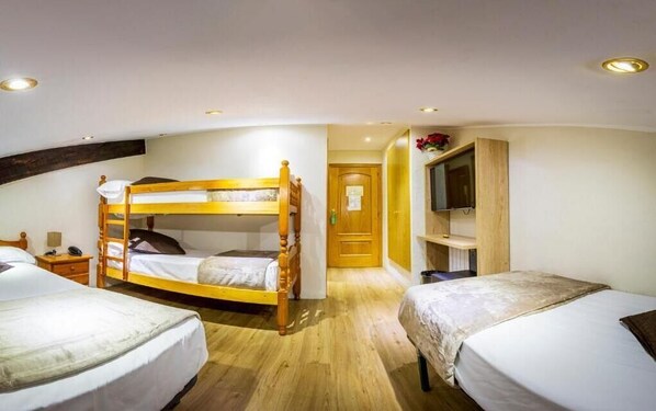 Una habitación con dos camas individuales, una litera, un armario de madera, un televisor y una puerta que da a otra habitación.