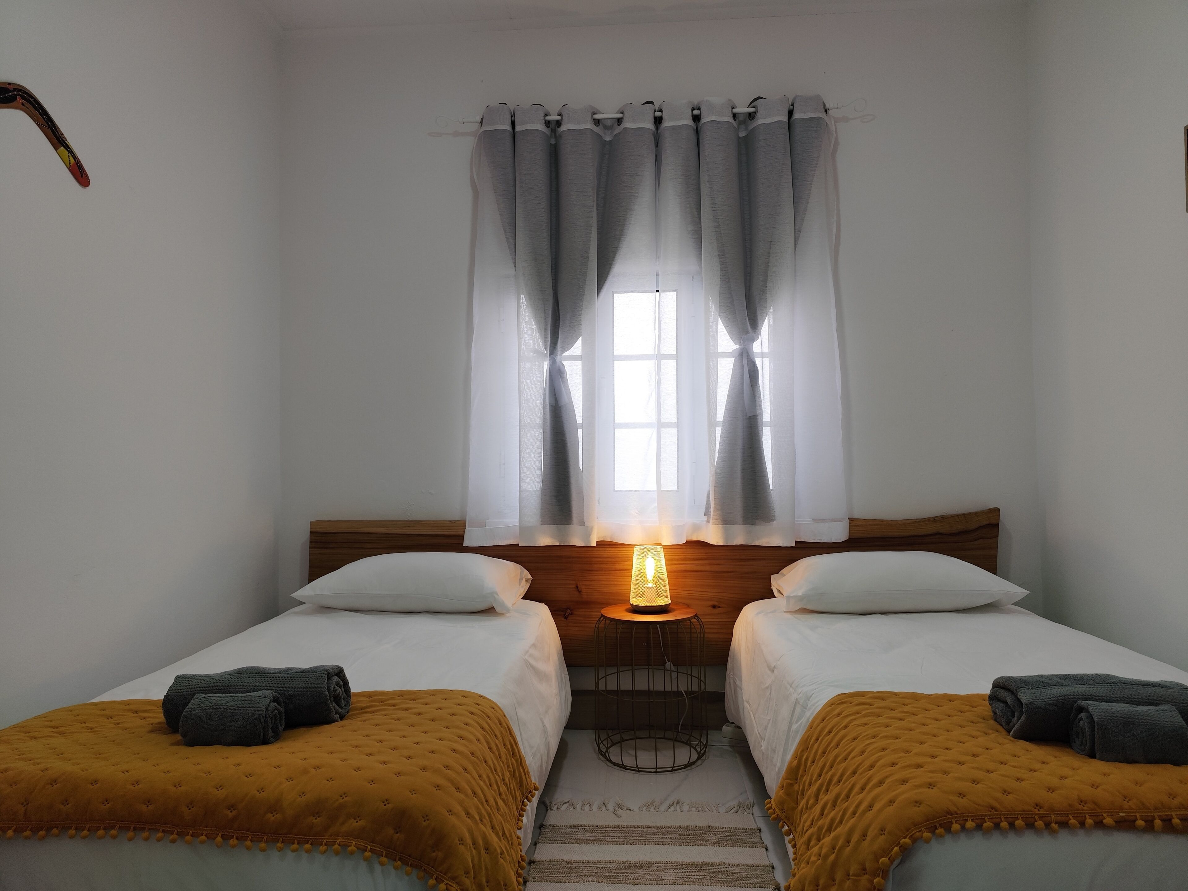 A room with two beds, a window with curtains, a bedside lamp, and a small round table.
