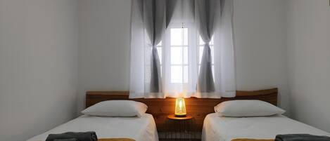 A room with two beds, a window with curtains, a bedside lamp, and a small round table.