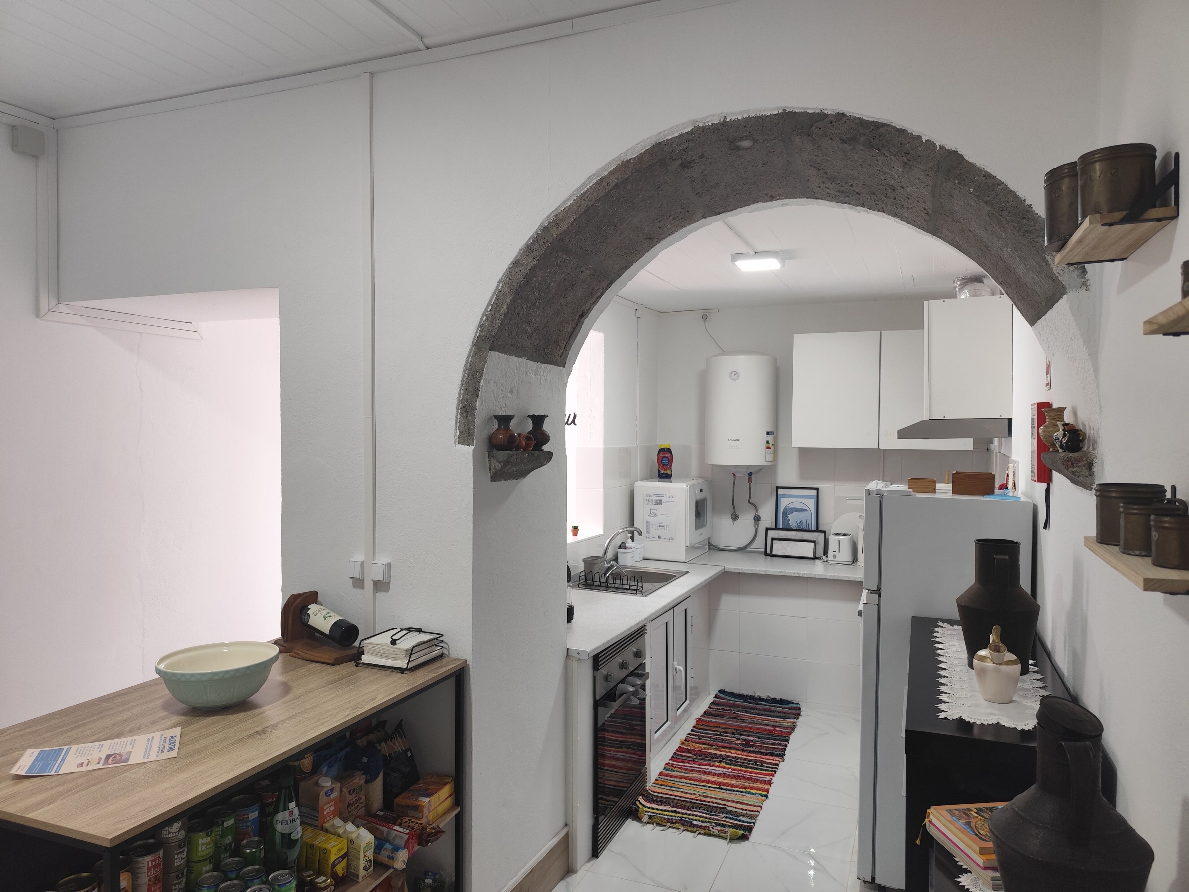A kitchen with white cabinets, a microwave, a refrigerator, and a wooden table with a bowl and a book.