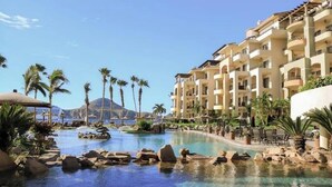 A resort with a swimming pool, palm trees, and a mountain in the background.