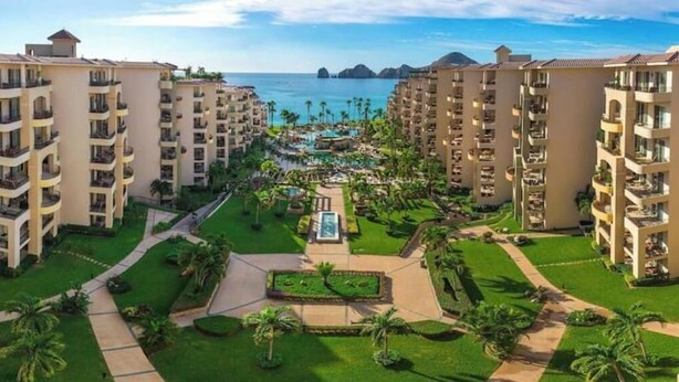 A resort with multiple high-rise buildings, a central pool area, and a view of the ocean.