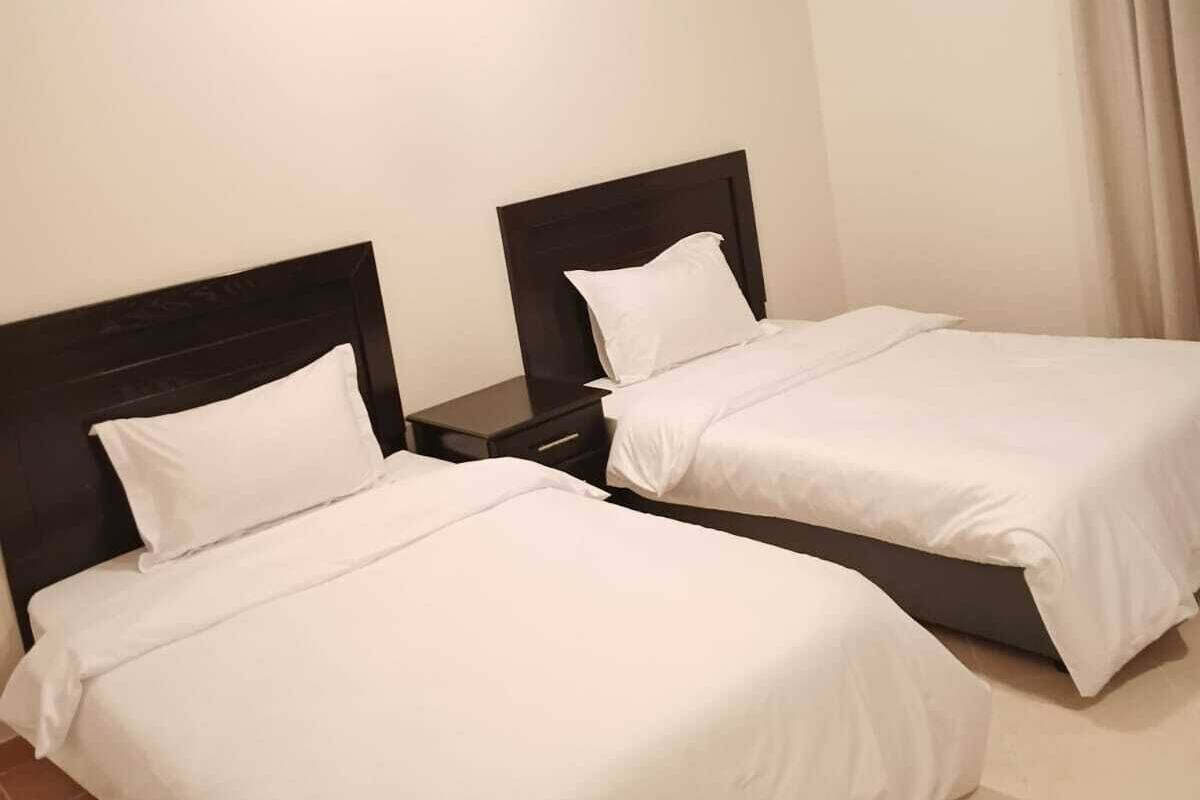 A hotel room with two single beds, a nightstand, a ceiling light, and a window with curtains.