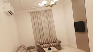 A living room with a sofa, a smaller couch, a coffee table, a TV mounted on the wall, and a ceiling light fixture. - Rama Dubai Serviced Apartments 4 (Riyadh)