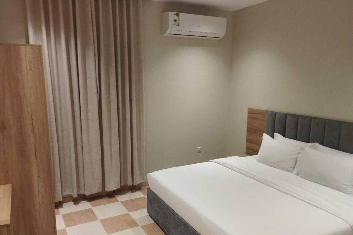 A hotel room with a bed, curtains, an air conditioning unit, and a checkered floor.