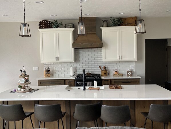 A modern kitchen with white cabinets, a large island, and hanging pendant lights.
