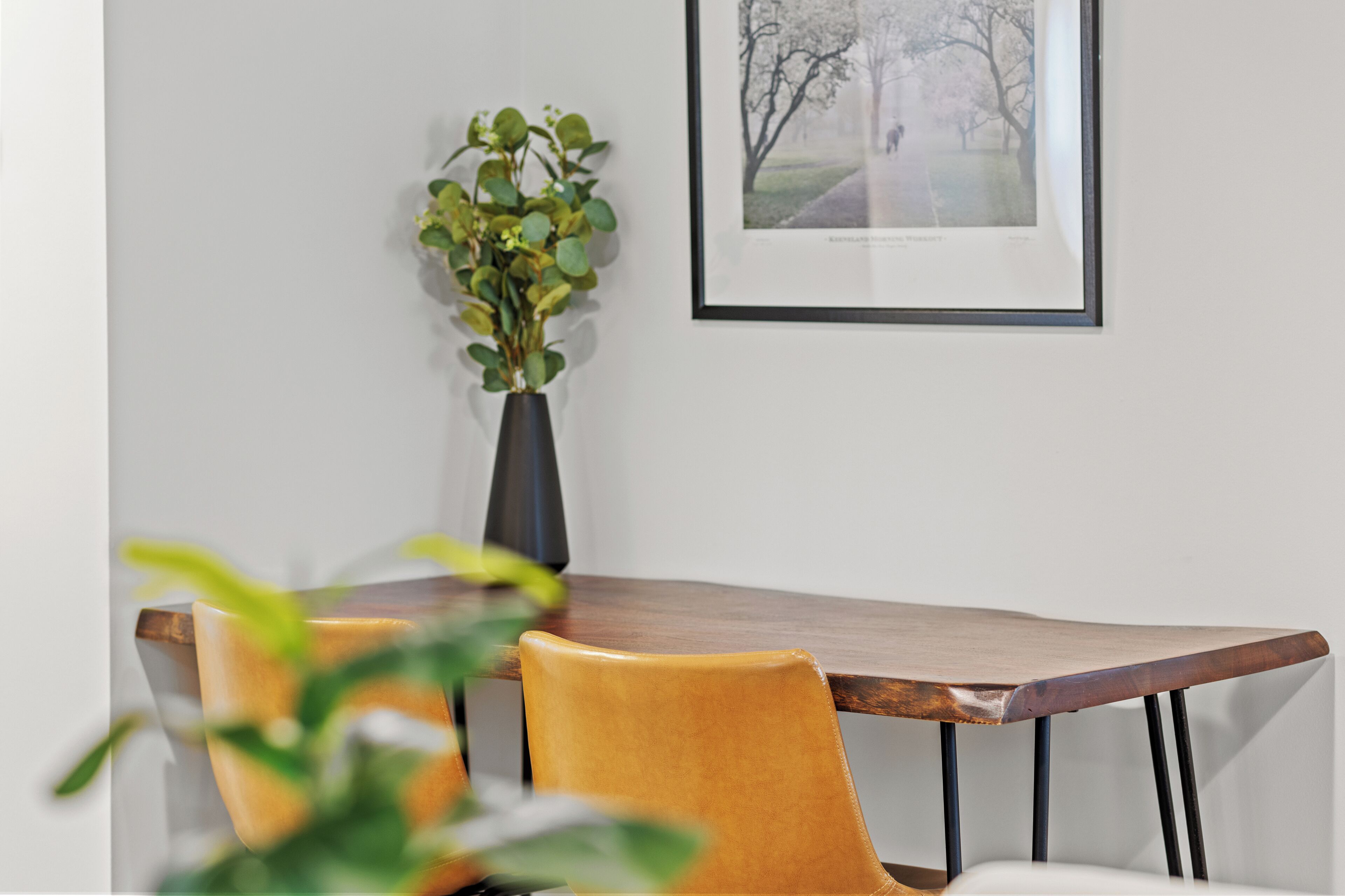 Un coin repas avec une table en bois et deux chaises jaunes. Un vase contenant des feuilles vertes est posé sur la table.