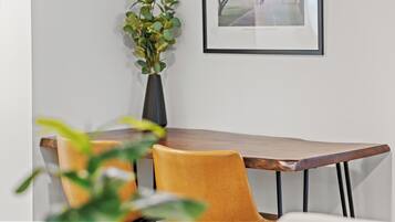 Un coin repas avec une table en bois et deux chaises jaunes. Un vase contenant des feuilles vertes est posé sur la table.
