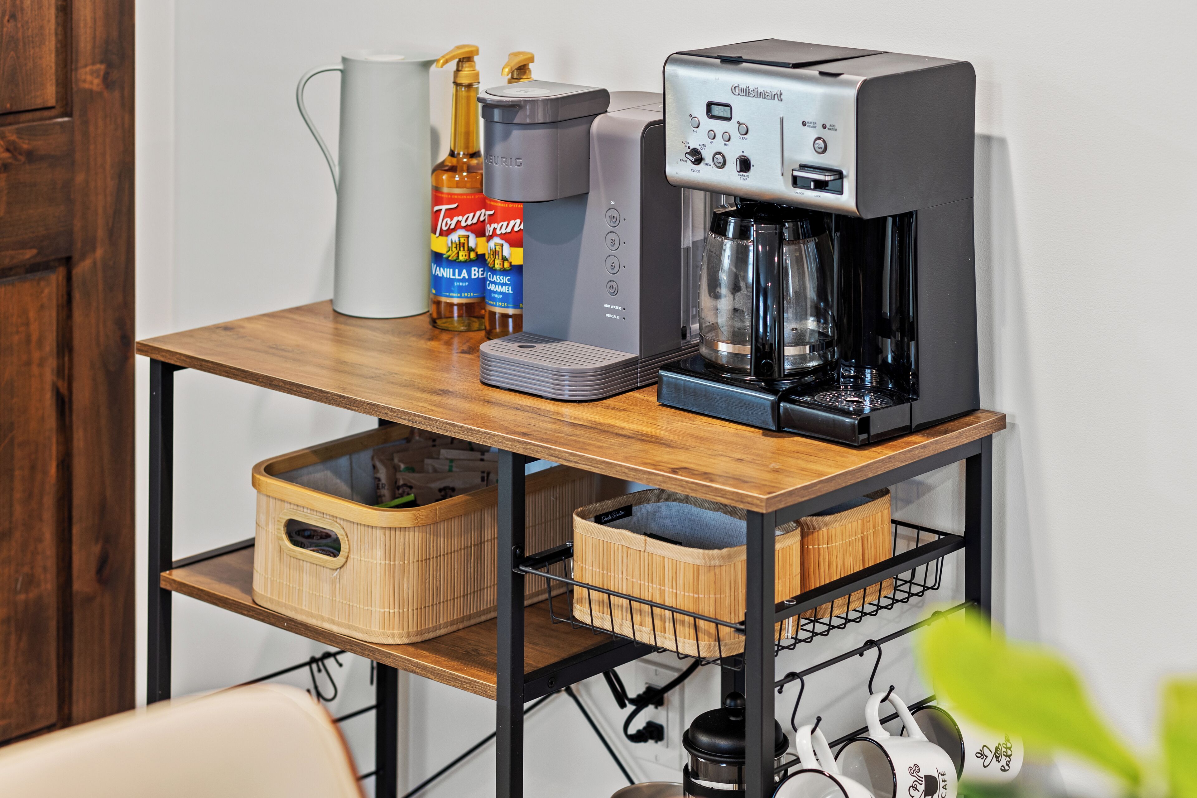 Une machine à café, un pichet et une bouteille de sirop Torani sur une table en bois.