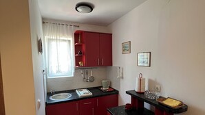 Una cucina compatta con mobili rossi, un piano di lavoro nero e una finestra con tende leggere.