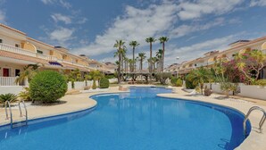 Una piscina de diseño curvo, rodeada de palmeras y una zona de estar techada.