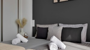 Una cama bien hecha con toallas blancas enrolladas, un jarrón con plumas de plumas de pampa secas y un cuadro abstracto enmarcado en la pared.