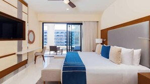 Habitación de hotel con una cama grande, televisión, ventilador de techo y vista a la ciudad desde la ventana.