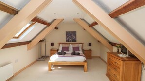 Een slaapkamer met een schuine kap, een bed, een dressoir en een nachtkastje.