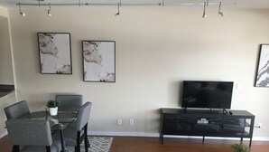 Un salon moderne comprenant un coin repas, un meuble de rangement noir pour les appareils multimédias et deux œuvres d’art encadrées accrochées au mur.