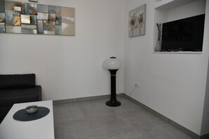 Un salon moderne avec un canapé blanc, une table basse surmontée d’un bol décoratif, un lampadaire et des œuvres d’art abstraites accrochées au mur.