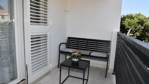 A balcony with a black metal bench, a small table with a flower vase, and a white door with blinds. - A1 Apartment With Terrace, 1 min Walk to the Beach (Supetar)