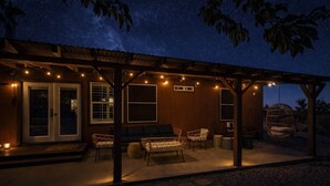 A covered outdoor seating area with string lights, a swing, and a view of the night sky. - Navigate Stays Pet Friendly Desert Dream (Yucca Valley)