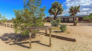 A desert landscape with a wooden signpost, a building, and sparse vegetation. - Navigate Stays Pet Friendly Desert Dream (Yucca Valley)