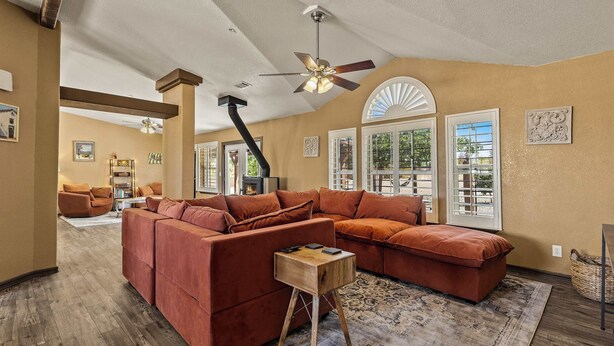 A spacious living room with a large sectional sofa, a wooden side table, and a ceiling fan. - Navigate Stays Pet Friendly Desert Dream (Yucca Valley)