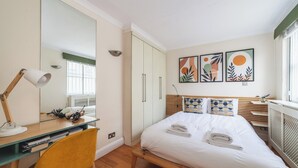 Ein Schlafzimmer mit Bett, Schreibtisch, Stuhl, Kleiderschrank und Bildern an der Wand.