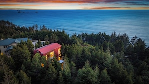 A coastal property with a prominent red building surrounded by dense forest, overlooking the sea. - Port Orford Ocean View, Waterfront & BBQ Area (Port Orford)
