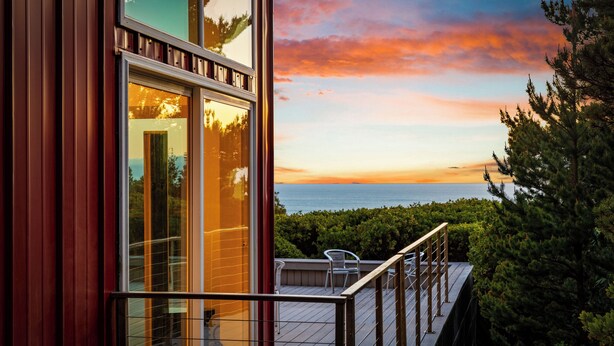 A balcony with a view of the sea at sunset, a glass door, and a railing. - Port Orford Ocean View, Waterfront & BBQ Area (Port Orford)
