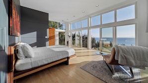 A modern bedroom with a large bed, a seating area with a towel, and a balcony with a view of the sea. - Port Orford Ocean View, Waterfront & BBQ Area (Port Orford)