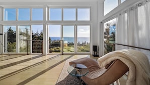 A spacious room with large windows, a glass coffee table, and a brown sofa. - Port Orford Ocean View, Waterfront & BBQ Area (Port Orford)