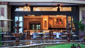 An outdoor dining area with tables and chairs, a fountain, and a building entrance with a sign.