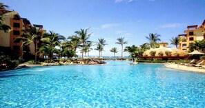 Une grande piscine aux eaux cristallines, entourée de palmiers et des bâtiments de l’hôtel.