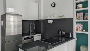 A modern kitchen with white cabinets, a black countertop, a Bosch refrigerator, a sink, a clock, and a coffee machine.