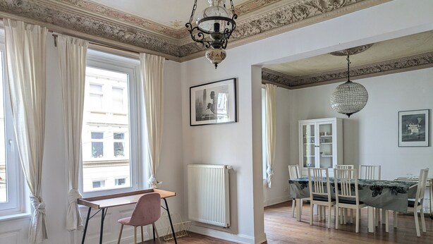 A room with a dining area, a table with chairs, a radiator, and a window with curtains.