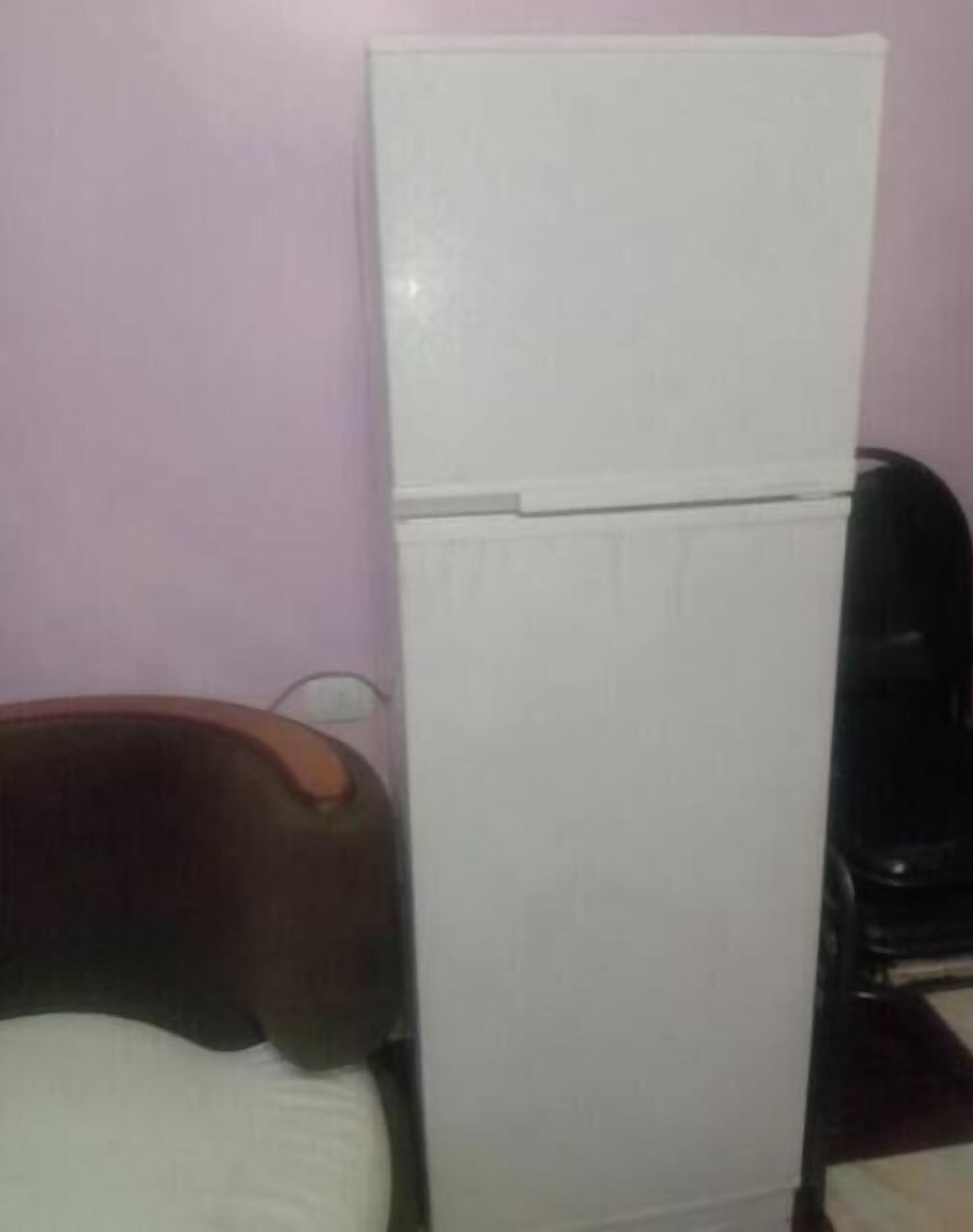 A small room with a bed, a white refrigerator, and a black chair.