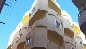 Un immeuble à plusieurs étages doté de balcons, une enseigne indiquant un espace public et un ciel dégagé.