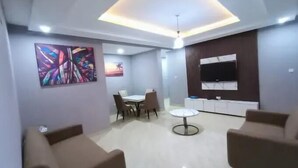 A modern living room with a dining area, a TV mounted on the wall, and a ceiling light fixture. - Kosy Stay Apartment (Abuja)
