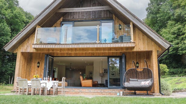 Una casa in legno a due piani con un balcone, una zona pranzo con posti a sedere all'aperto e un'ampia finestra.