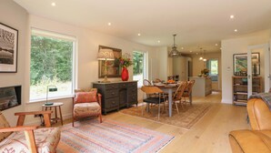 Un soggiorno spazioso con un grande tappeto, un'area pranzo con tavolo e sedie in legno, una cucina con elettrodomestici moderni e vista sul verde.